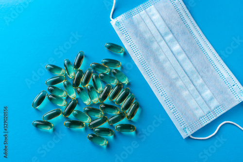 Surgical mask and a scattering of yellow fish oil capsules on a blue background. medical background photo