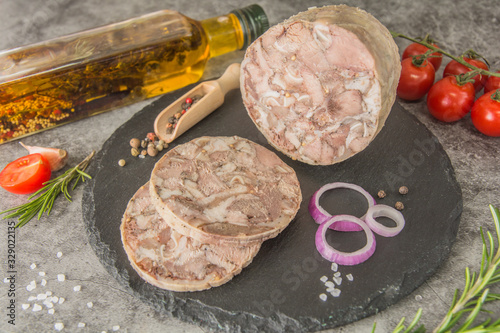 Headcheese is a pressed pressed piece of meat cut on black slate. Close-up, with spices, rosemary, tomato. Dish on the menu.