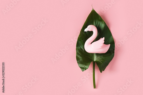 Creative pastel falt lay with tropical leaves and mini flamingo on pink background photo