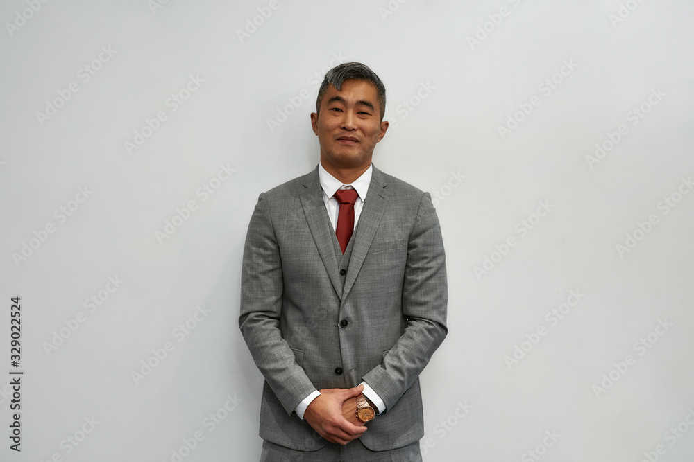 Confidence and success. Portrait of successful asian businessman in classic wear looking at camera and smiling while standing against grey background Confidence and success. Portrait of successful asian businessman in classic wear looking at camera and smiling while standing against grey background