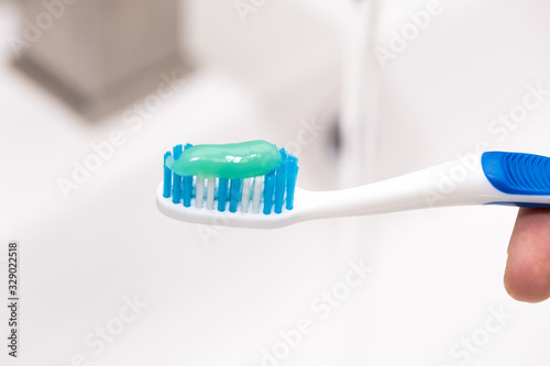 Toothbrush with toothpaste in the guy's hand on the background of the washbasin.