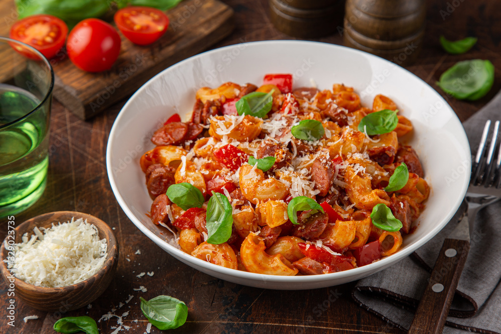 Spicy sausages marinara pasta with parmesan cheese and fresh basil in white bowl Spicy sausages marinara pasta with parmesan cheese and fresh basil in white bowl
