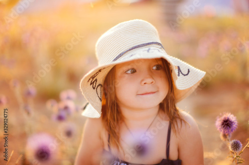 Child girl in straw hat flowers on sandy beach