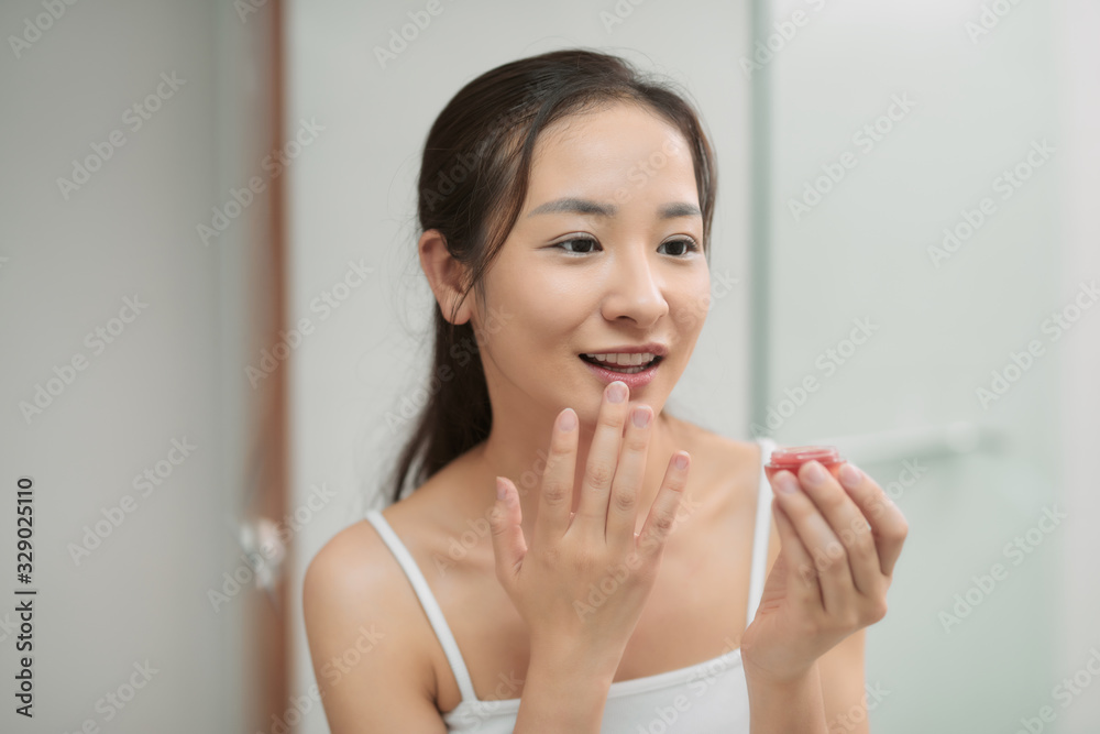a young woman is painting lip balm in bathroom at home a young woman is painting lip balm in bathroom at home
