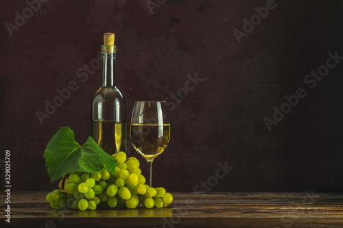 Glasses and bottles of white wine and grapes on dark claret bordeaux concrete surface background.