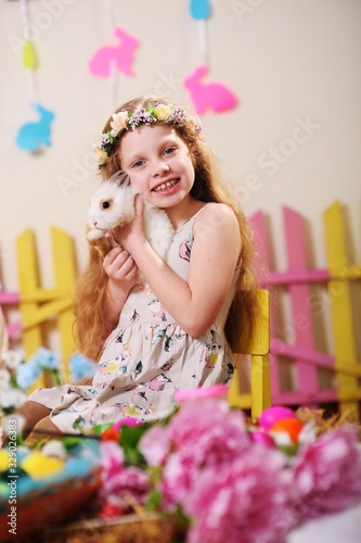 child-a little girl in a dress and a flower wreath on her head smiling and holding an Easter Bunny on the background of flowers and decor