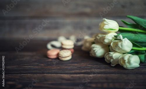 Spring flowers. Bouquet of white tulips and macaroons on brown wooden table. Mother's Day and Valentines Day background. Rustic style. Copy space for your text.