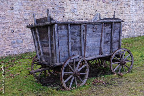 The broken ancient medieval rural wood cart or wagon on the green grass on the background of the castle or fortress stone or brick wall 