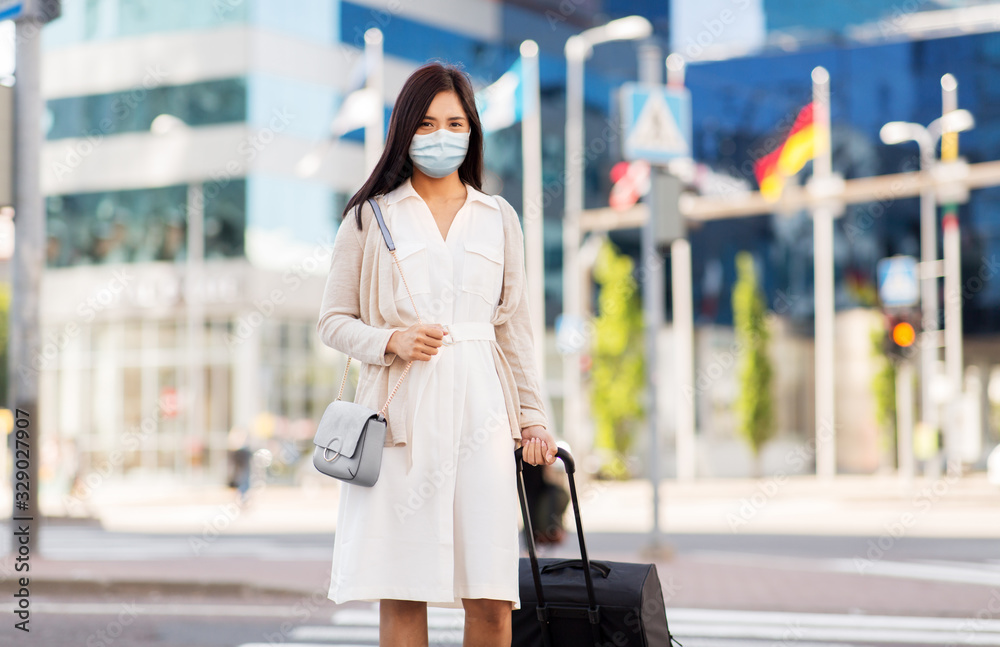 Fototapeta premium health, people and tourism concept - happy young asian woman wearing protective medical mask for protection from virus with travel bag on city street