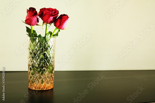 Three red roses in glass vase on white background