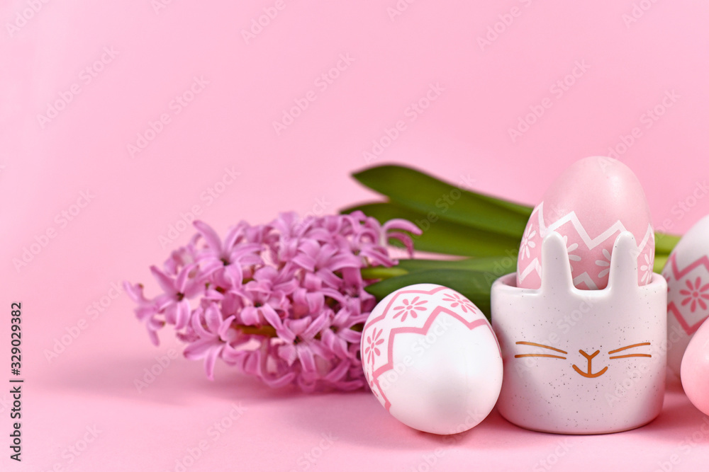 Pink and white painted easter eggs and cute easter egg cup in shape of bunny with Hyacinth spring flower on pink background