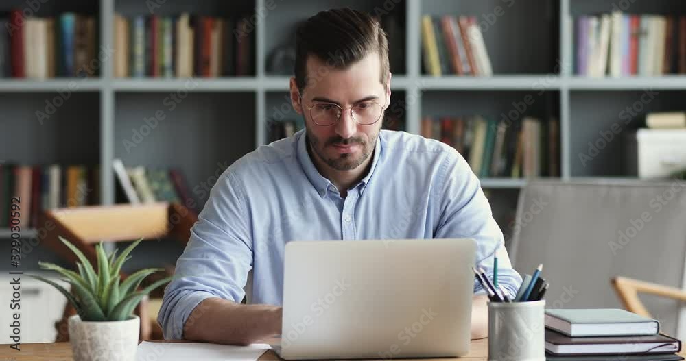 Focused business man entrepreneur typing on laptop doing research. Young male professional using computer sitting at home office desk. Busy worker freelancer working on modern tech notebook device.