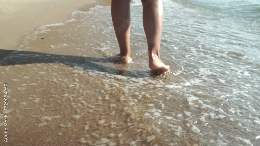 On a Tropical Beach Beautiful Scene of a Woman Walking on Ocean Beach at Sunset. Close-Up of Women's Legs Walking Along the Beach On a Tropical Beach Beautiful Scene of a Woman Walking on Ocean Beach at Sunset. Close-Up of Women's Legs Walking Along the Beach