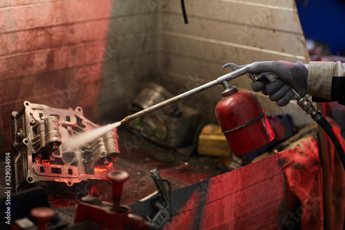 Unrecognizable man sandblasting car motor part to clean it, horizontal shot, copy space