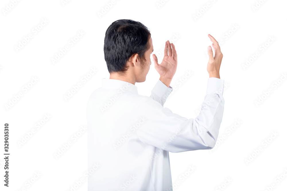 Rear view of Asian Muslim man standing while raised hands and praying