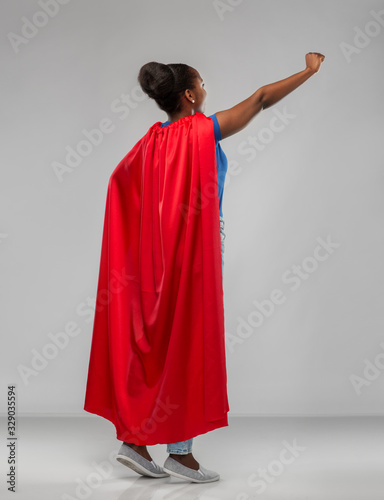 women's power and people concept - happy african american woman in red superhero cape over grey background