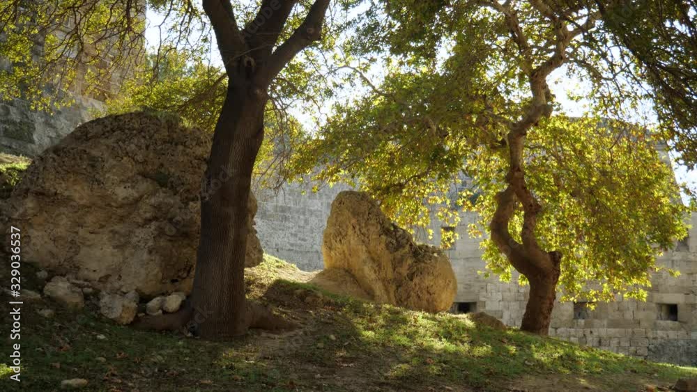 Boulders under trees by the stone walls of Rodos Town, Greece Boulders under trees by the stone walls of Rodos Town, Greece