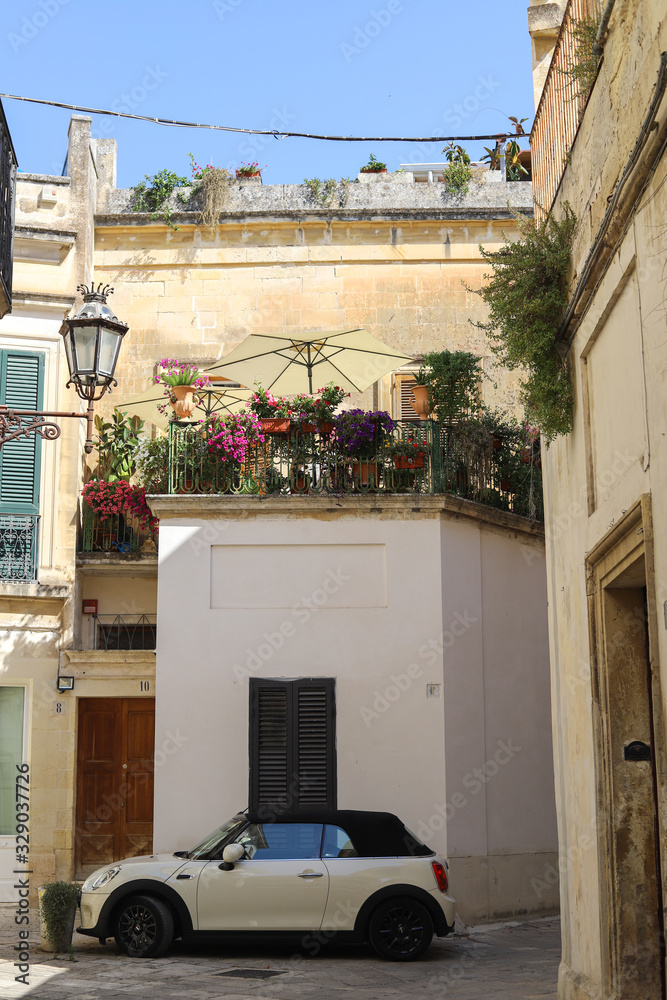 Italian cozy courtyard with a terrace, flowers, street light, white walls and a white mini car