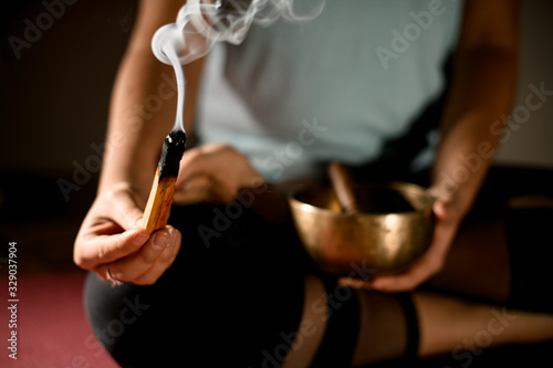 Young woman sitting in yoga pose and holding smoldering stick.