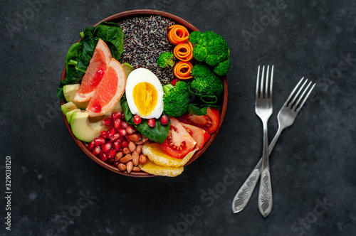 Bowl of Buddha,quinoa, orange, avocado, grapefruit, tomato, pomegranate, spinach, carrots, broccoli, egg in a bowl on a stone background.