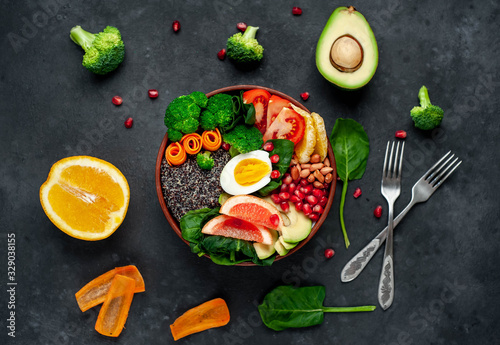 Bowl of Buddha,quinoa, orange, avocado, grapefruit, tomato, pomegranate, spinach, carrots, broccoli, egg in a bowl on a stone background.