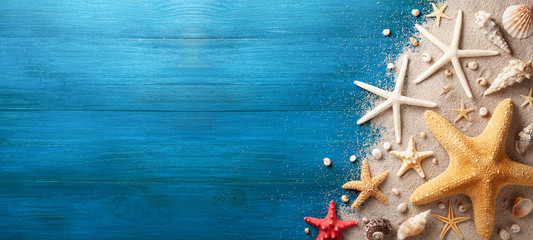 Seashell, starfish and beach sand on blue wooden background. Summer holiday banner. Top view.