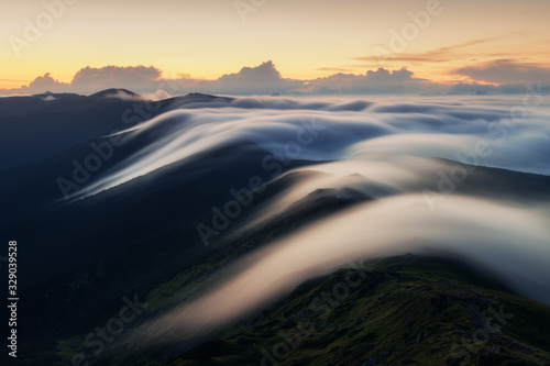 Amazing flowing morning fog in spring mountains blurred from long exposure. Beautiful sunrise on background. Landscape photography