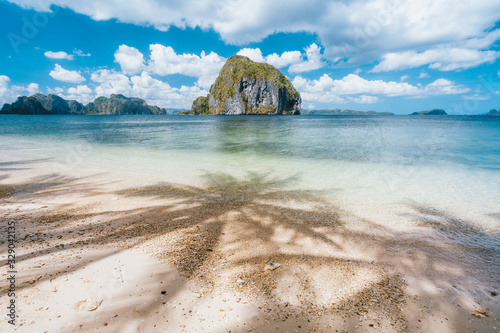 Fototapeta Naklejka Na Ścianę i Meble -  Palms shadows on tropical beach Las cabanas. Unique amazing tropical island in background. Beautiful landscape scenery in El Nido, Palawan, Philippines