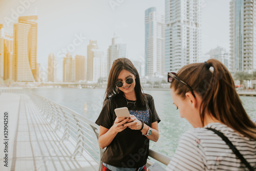 Photography Two attractive girls are standing in Dubai Marina and using a mobile phone