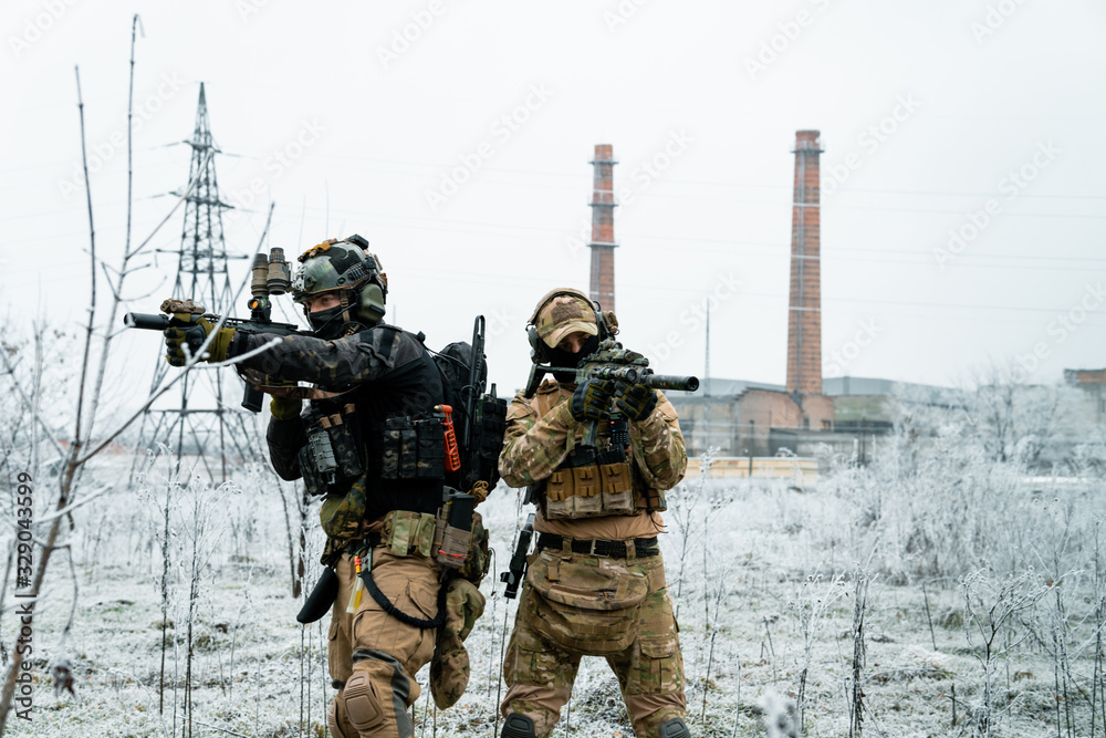 Men in camouflage cloth and black uniform with machineguns side to side with factory on background. Soldiers with muchinegun aims aiming Men in camouflage cloth and black uniform with machineguns side to side with factory on background. Soldiers with muchinegun aims aiming
