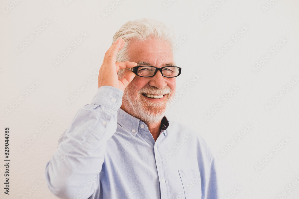 close up and potrait of mature man smiling and looking at the camera with a white wall at the background - active senior concept and lifestyle - intellectual and intelligence pensioner with glasses close up and potrait of mature man smiling and looking at the camera with a white wall at the background - active senior concept and lifestyle - intellectual and intelligence pensioner with glasses