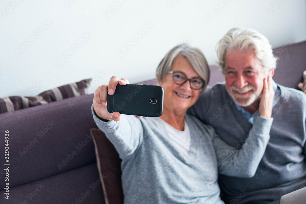 couple of two seniors at home on the sofa taking a selfie together - mature people smiling and looking at the camera of the phone to take a picture couple of two seniors at home on the sofa taking a selfie together - mature people smiling and looking at the camera of the phone to take a picture
