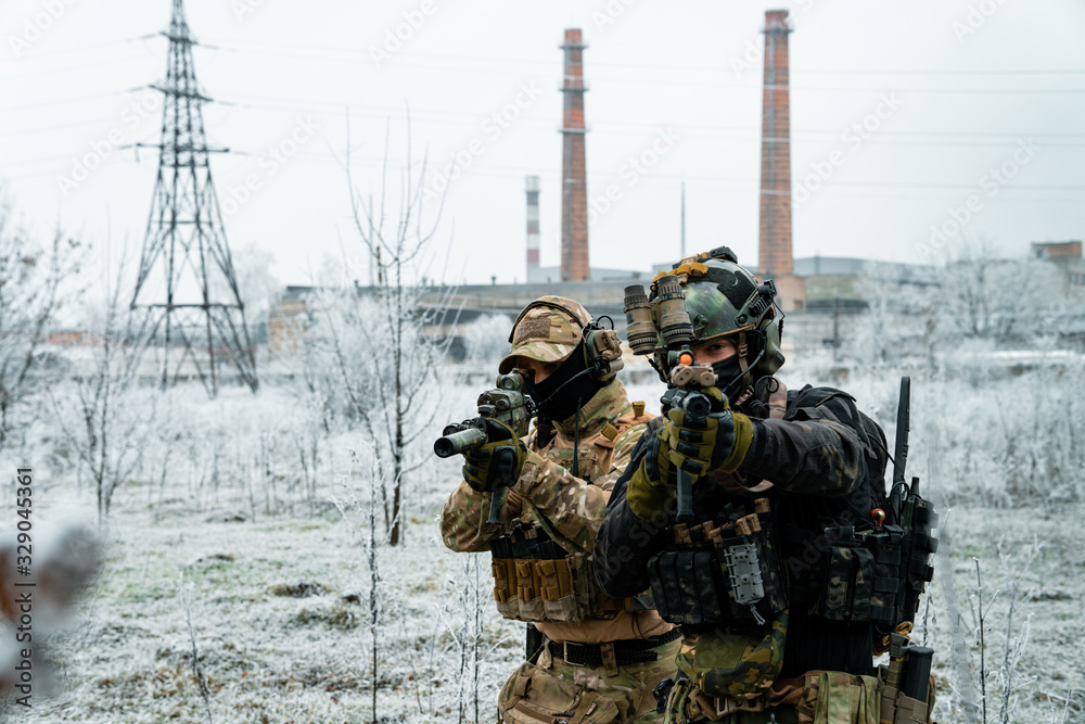 men in camouflage cloth and black uniform with machineguns side to side with factory on background. Soldiers with muchinegun aims aiming men in camouflage cloth and black uniform with machineguns side to side with factory on background. Soldiers with muchinegun aims aiming