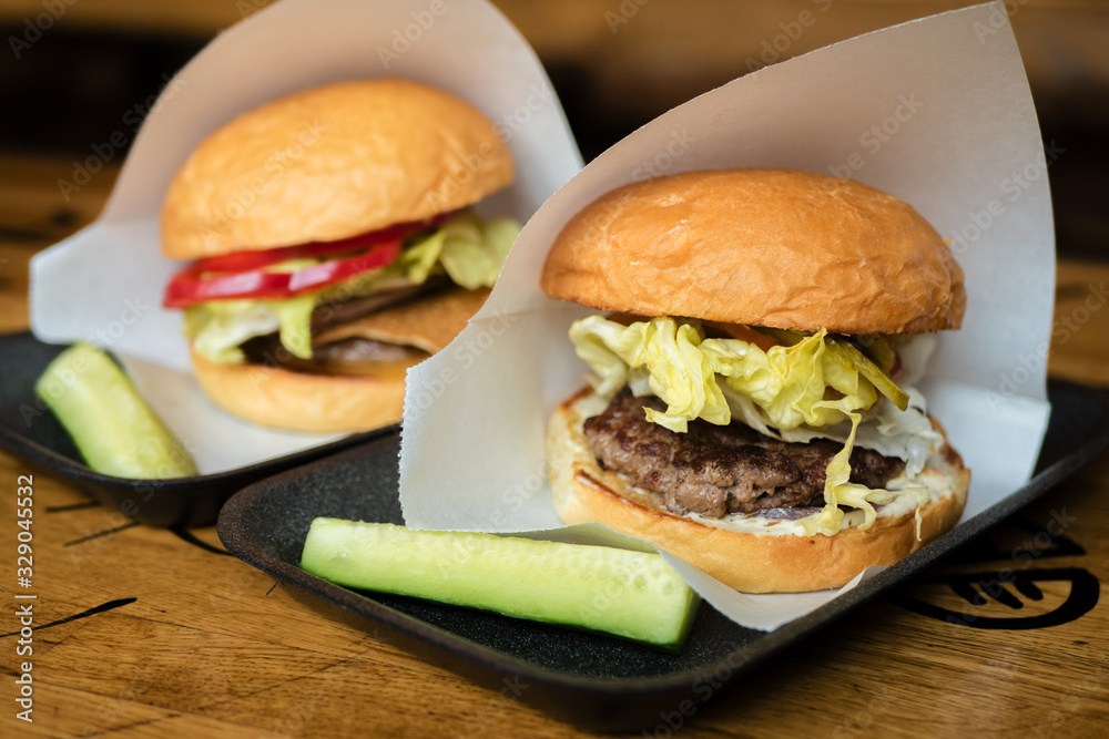 Two burgers with cutlet, cabbage and cucumber in white paper envelopes on the substrate.