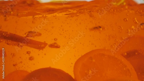 Fresh orange slices falling with splashes and bubbles into the orange water or tea against light background. The concept of a healthy and clean food, diet, detox, vegetarian food. Wide shot