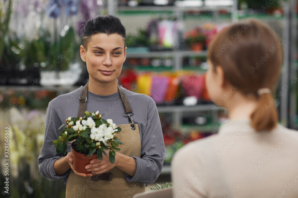 Waist up portrait of modern young woman selling flowers to customer in flower shop and smiling cheerfully, copy space Waist up portrait of modern young woman selling flowers to customer in flower shop and smiling cheerfully, copy space