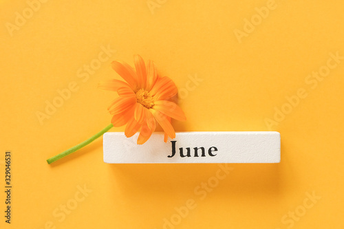 One orange calendula flower and calendar summer month June on yellow background. Top view Copy space Flat lay Minimal style. Concept Hello June Template for your design, greeting card