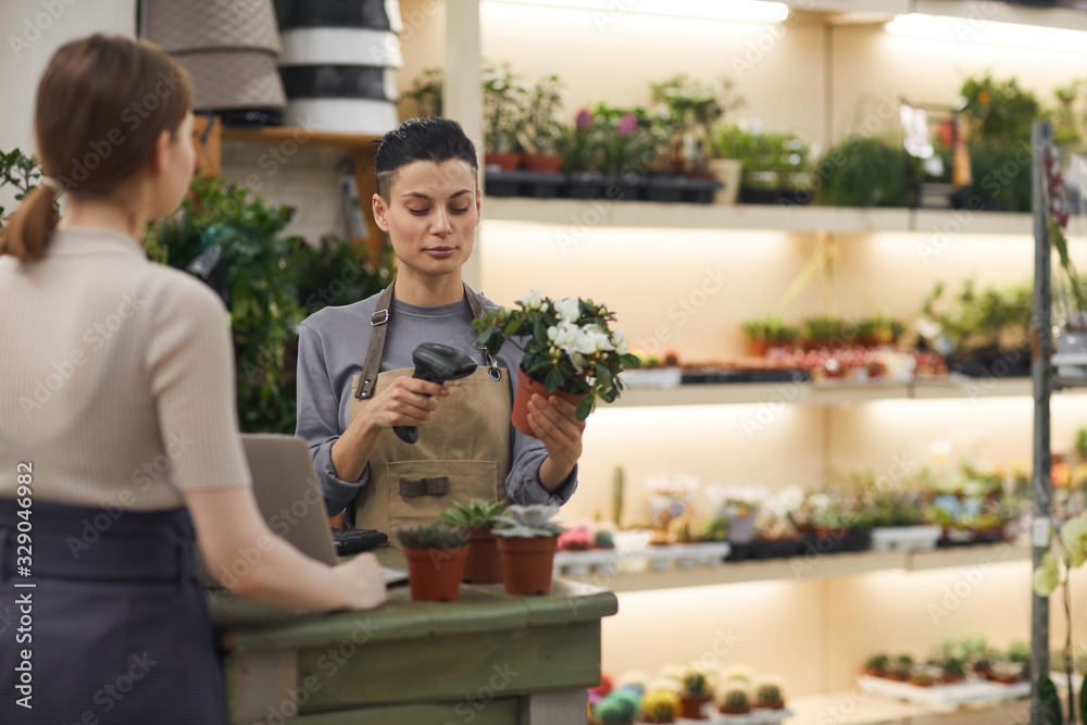 Waist up portrait of modern young woman selling flowers to customer in flower shop and scanning bar code, copy space Waist up portrait of modern young woman selling flowers to customer in flower shop and scanning bar code, copy space