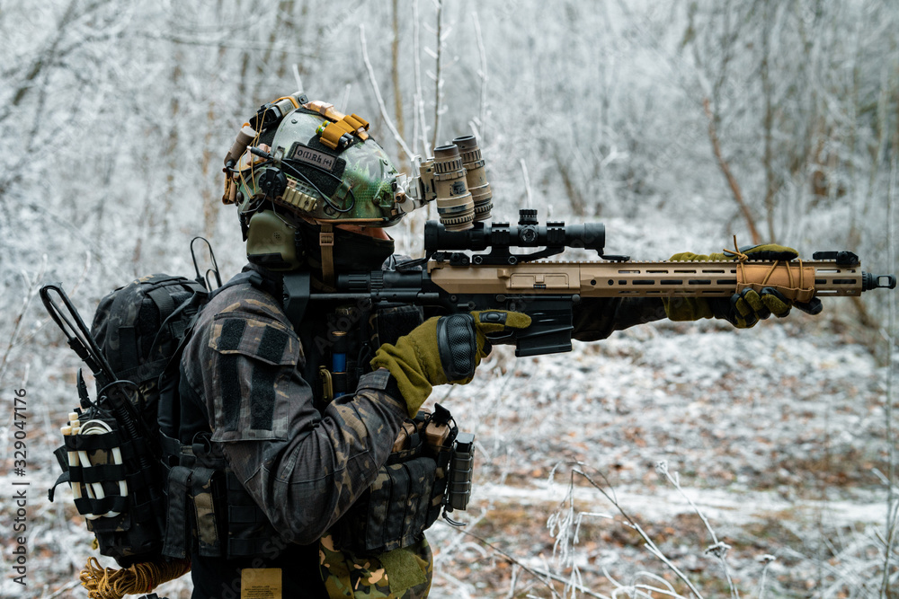Airsoft man in black camouflage uniform aims at the sight machinegun. Soldier in the winter forest. Vertical photo.