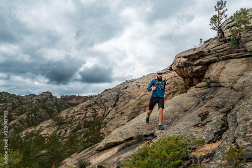 Runner runs on the rocky mountains. A man in blue jersey and black shorts is training outdoors