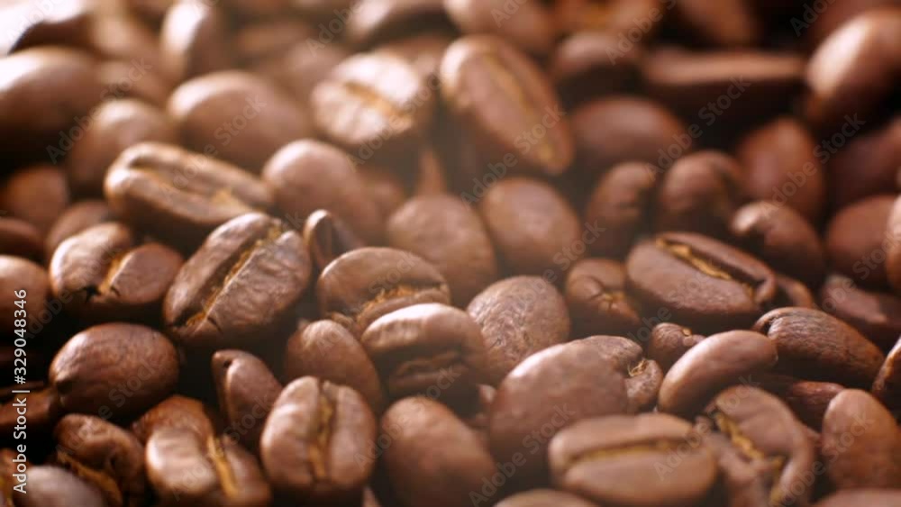 Roasted coffee beans rotate in a circle. Roasted coffee bean background, top view. Close-up of roasted coffee beans spinning slowly in a circle Roasted coffee beans rotate in a circle. Roasted coffee bean background, top view. Close-up of roasted coffee beans spinning slowly in a circle