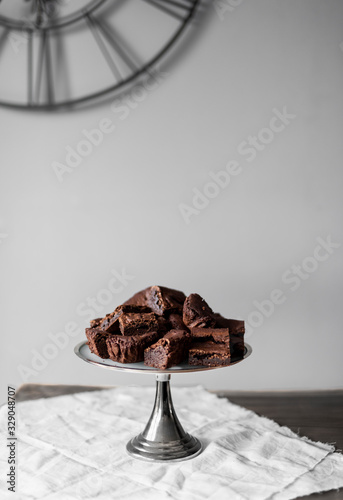 Pieces of chocolate brownie on a silver tart plate on white linen and wooden table photo