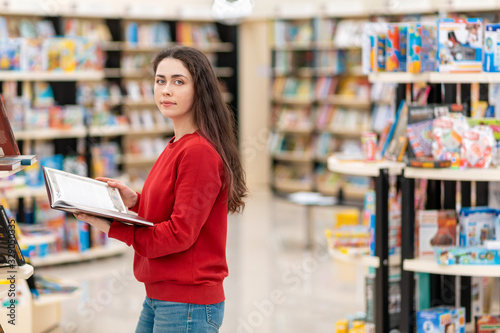 A young beautiful woman poses with a book in her hands, against the background of shelves with books. The concept of education and purchase of books