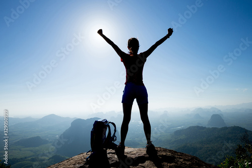Bilde på lerret Cheering woman backpacker enjoy the view on sunrise mountain top cliff edge