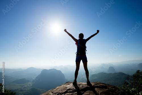 Foto Cheering woman backpacker enjoy the view on sunrise mountain top cliff edge