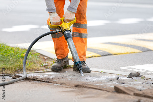 Builder worker breaking asphalt pavement with pneumatic construction hammer during road repairing works