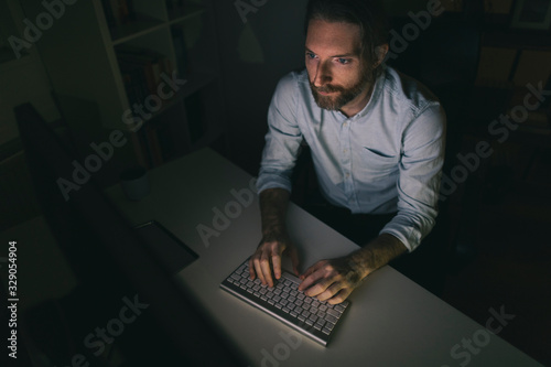 Bearded man working on computer long hours 