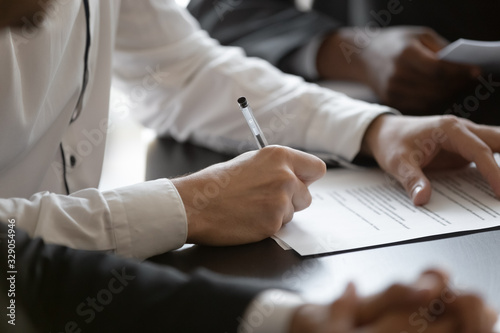 Close up young male employee manager customer hands signing paper contract after checking. Millennial investor client put signature at business agreement between partners. Editor making corrections. photo