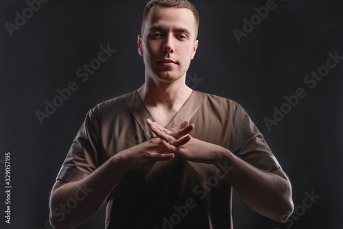 Young professional massage therapist flexes his hands before massage while standing against a dark background