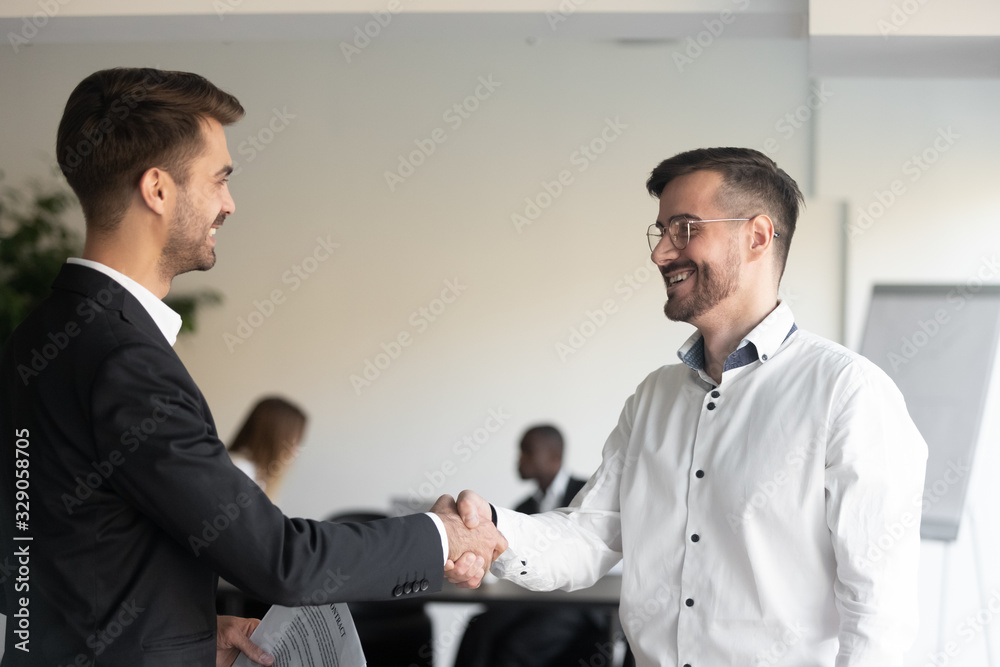 Two smiling business partners shaking hands with each other, celebrating good profitable deal. Happy executive getting acquainted to new corporate client. Hr manager welcoming new worker at office.